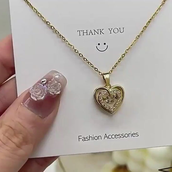 Gold heart-shaped necklace with a pendant on a gray surface video